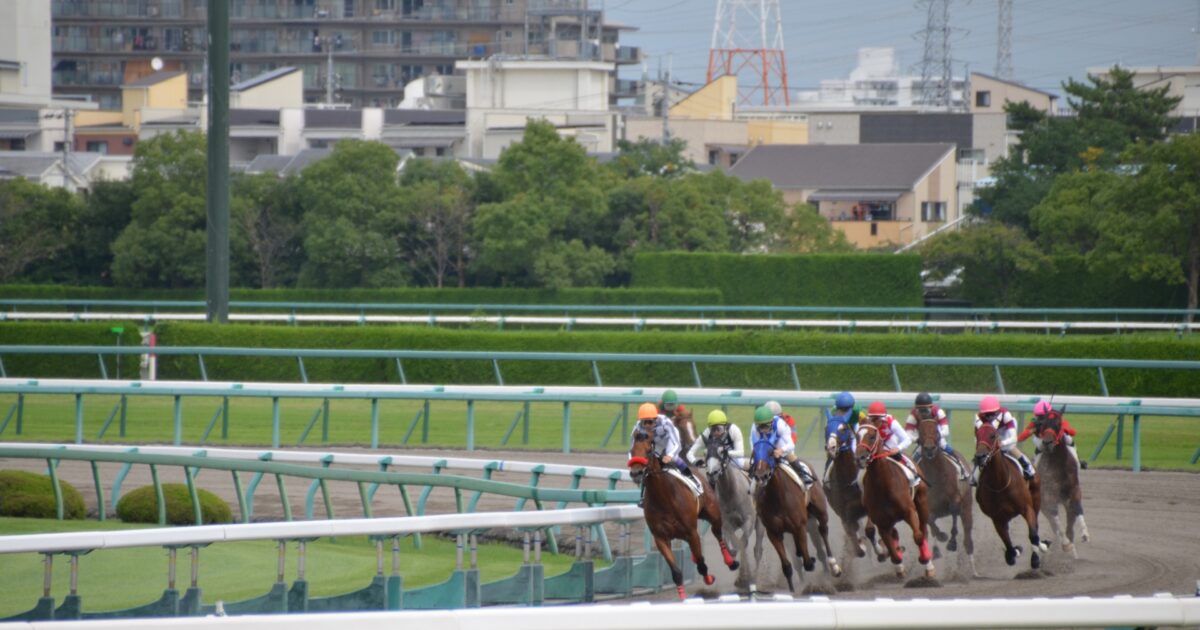 住宅街を背景にコーナーを駆け抜ける競走馬たち